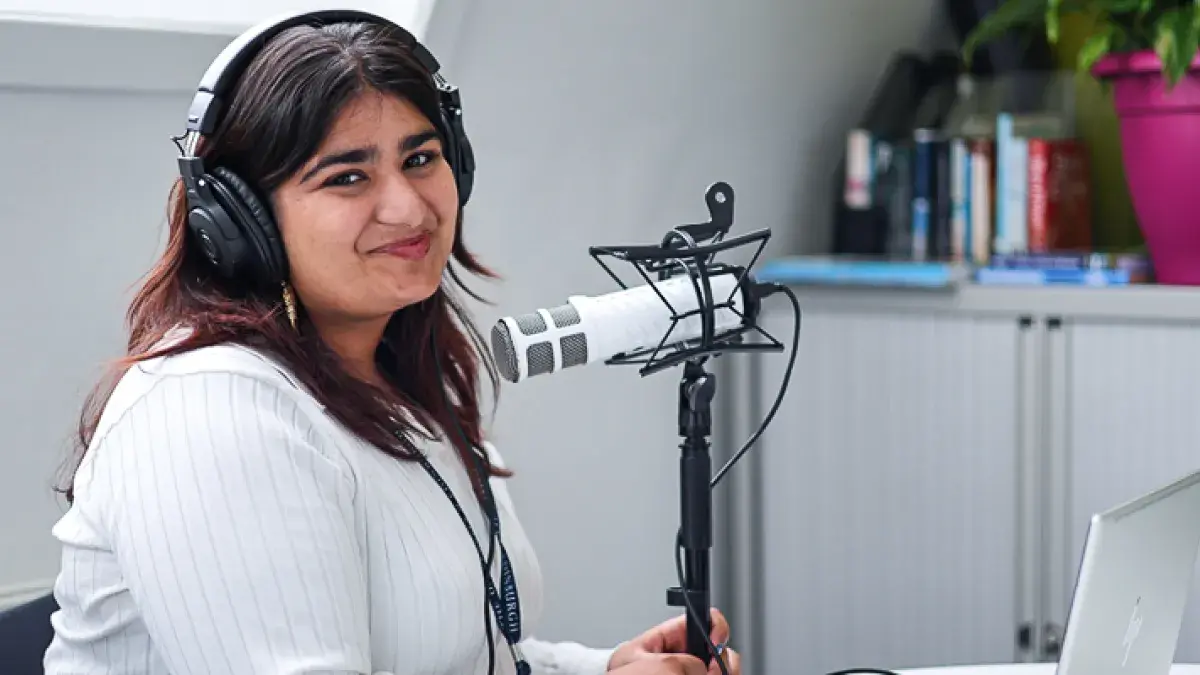 Nilufer Aumeerally Season 7 host photographed with a pod microphone, wearing headphones.