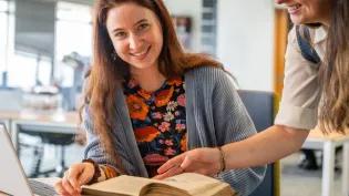 Two people discussing a Heritage Collections book that is open on the table.