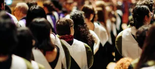 New alumni wearing graduation gowns are seated in McEwan Hall.
