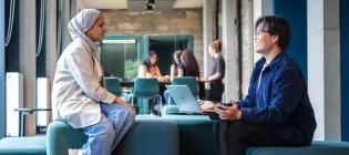 Two students are seated on stools facing each other, smiling and talking.