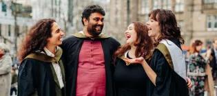 Four students wearing graduation gowns are talking and smiling.