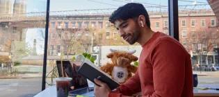 A student photographed studying in a New York café with Brooklyn Bridge in the background.