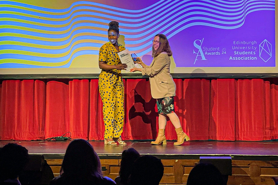 Beth Munro presents Forget Shareka with her Being Edinburgh Award on stage in 2024