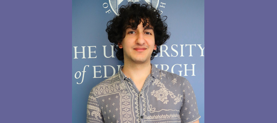 Ammir Barakat standing in front of the University of Edinburgh logo.