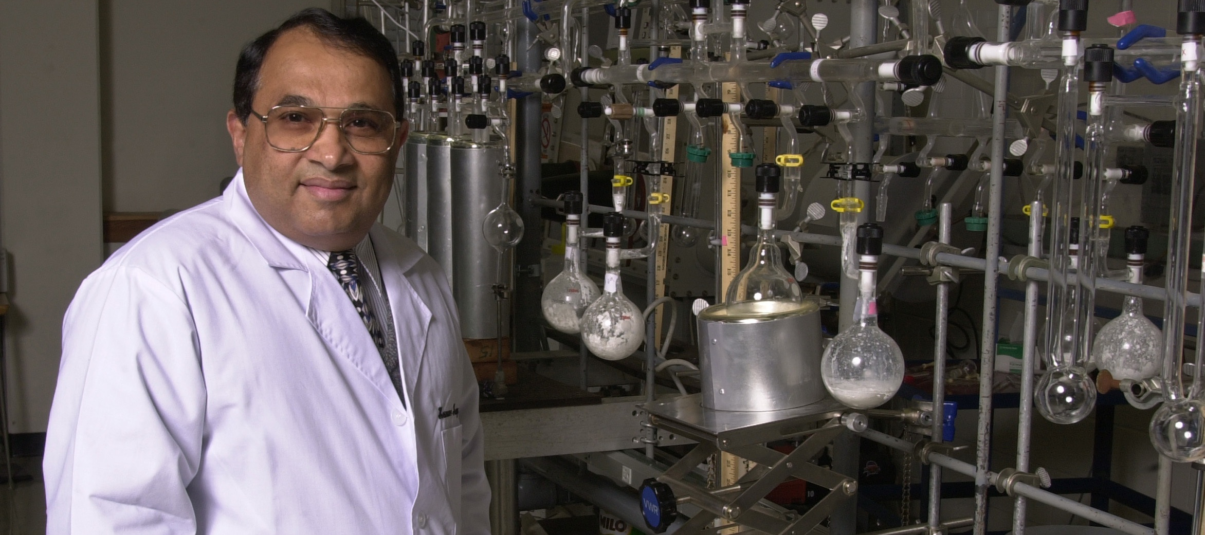 Narayan Hosmane stood in lab in front of test tubes, wearing a lab coat